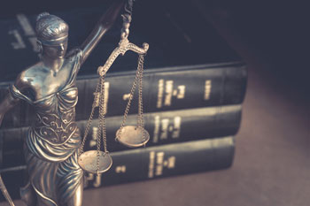 Ein Justitia-Modell und ein Stapel Gesetzesbuecher auf dem Schreibtisch eines Wirtschaftsrecht Absolventen